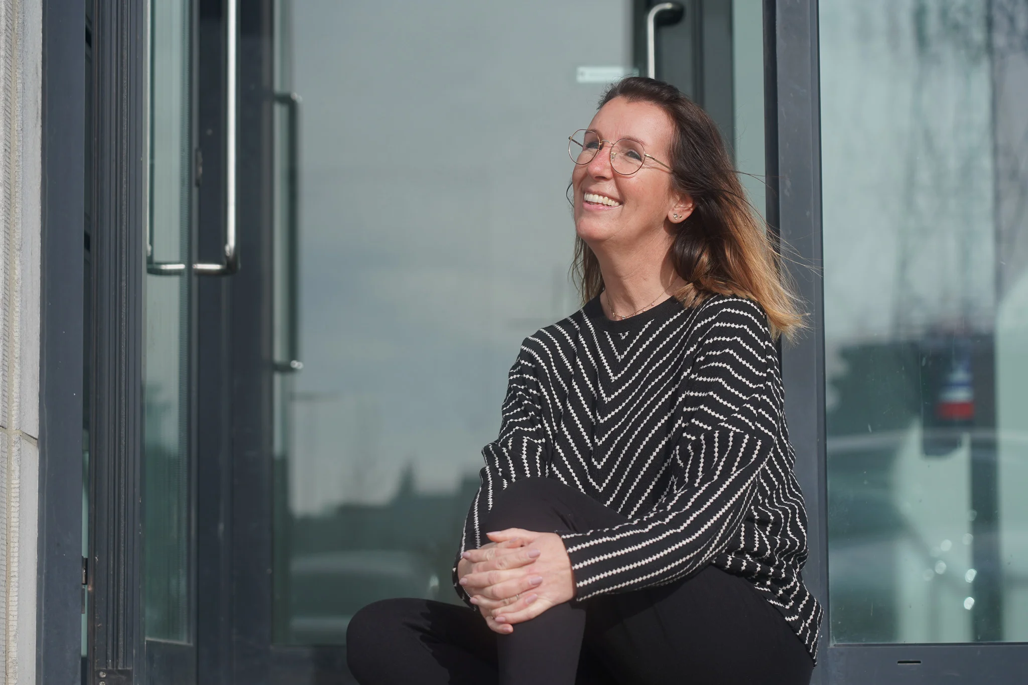 Woman smiling outside a building in the sunlight.